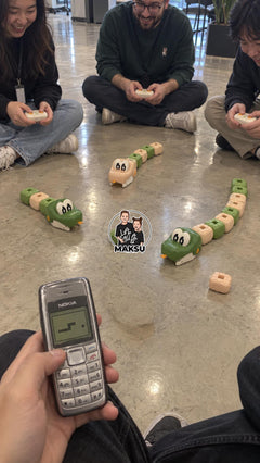 Adults sitting on the floor racing green and cream RC magnetic snakes next to an old Nokia phone with the Snake game — 6